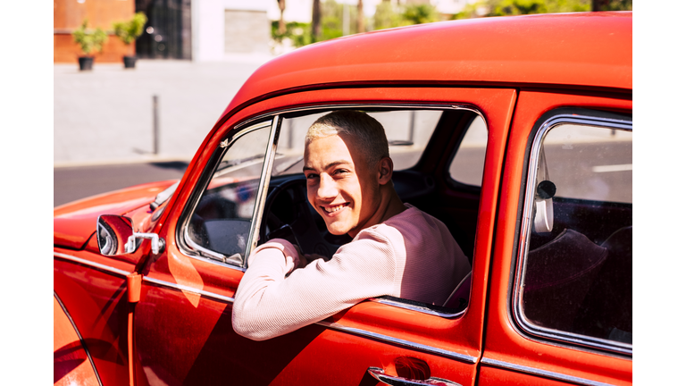 Portrait of happy teenage boy sitting in vintage car looking out of window