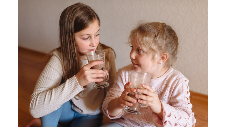 Two sisters hold glasses of hot chocolate in their hands.