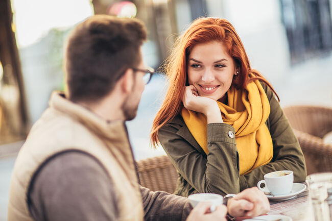 Attractive young couple in love sitting at the cafe table outdoors, drinking coffee