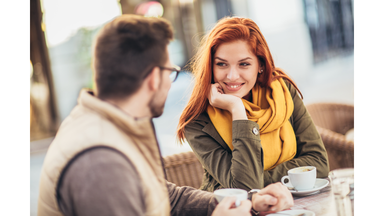 Attractive young couple in love sitting at the cafe table outdoors, drinking coffee
