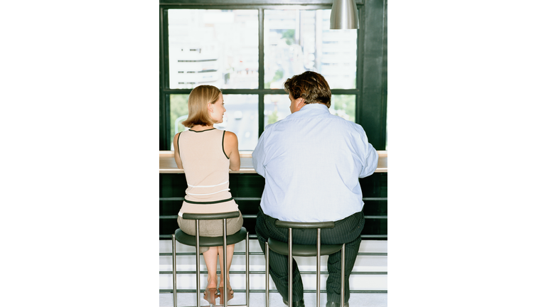 Petit woman and overweight businessman at table, rear view