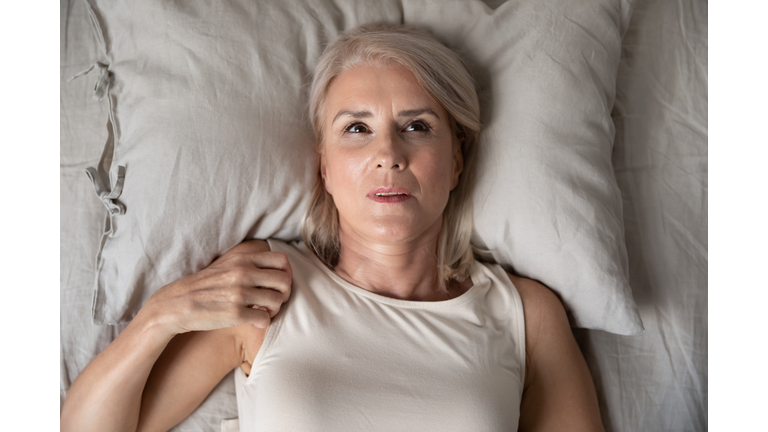 Middle aged woman insomniac lying awake in bed, top view