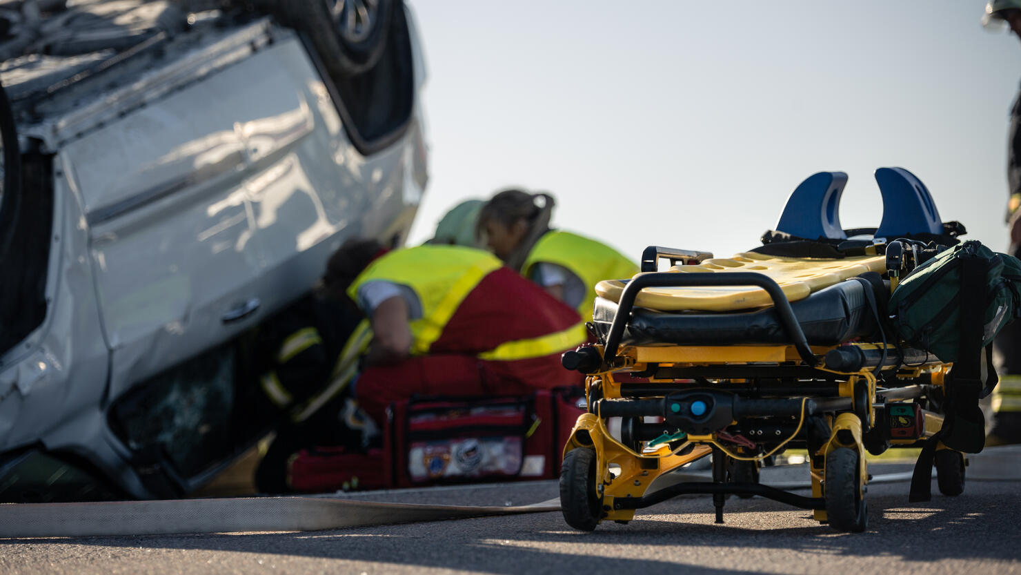 Paramedics and Firefighters Arrive On the Car Crash Traffic Accident Scene. Professionals Rescue Injured Victim Trapped in Rollover Vehicle by Extricating Them, giving First Aid and Extinguishing Fire