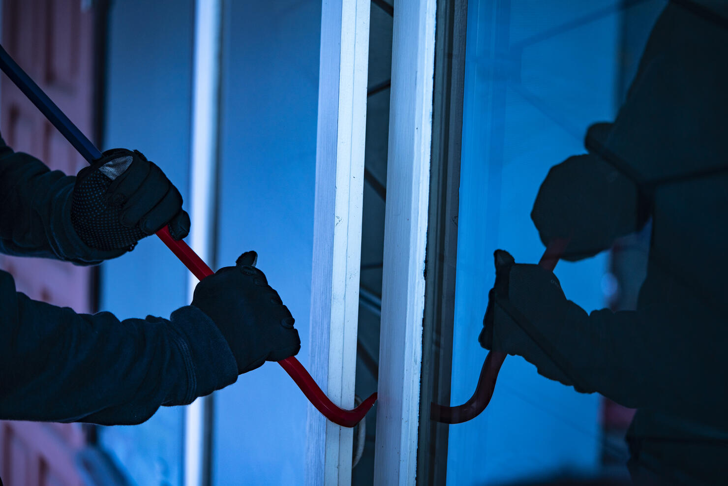 Burglar with crowbar trying break the door to enter the house