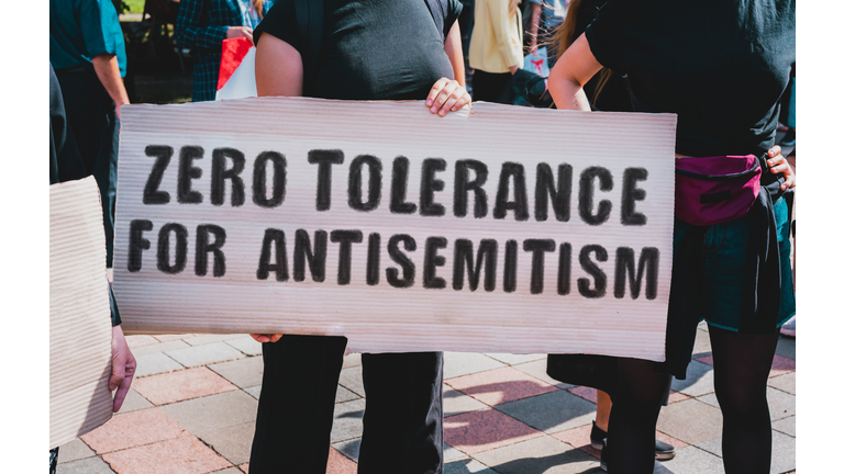 The phrase " Zero tolerance for antisemitism " drawn on a carton banner in hand. A girl holds a cardboard with an inscription. Girls on the street. Protest, march. Rally.