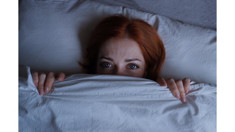 Sleepless Woman Lying In Bed Hiding Under Duvet At Night