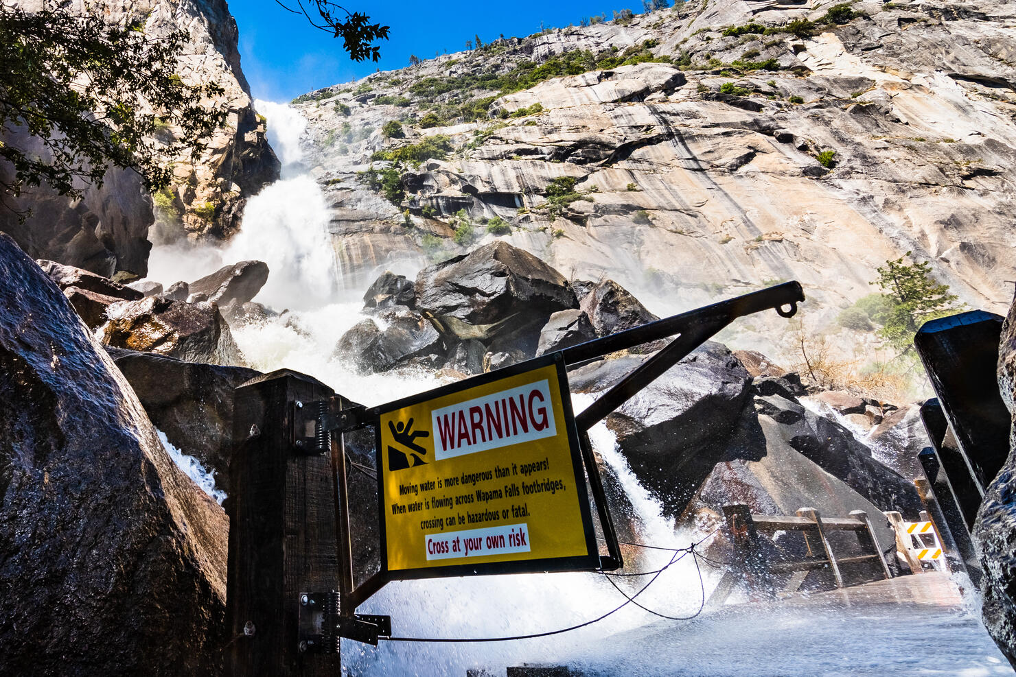 Warning sign due to Wapama Falls flowing over the footbridge and creating hazardous conditions for crossing; Hetch Hetchy Reservoir area, Yosemite National Park, California
