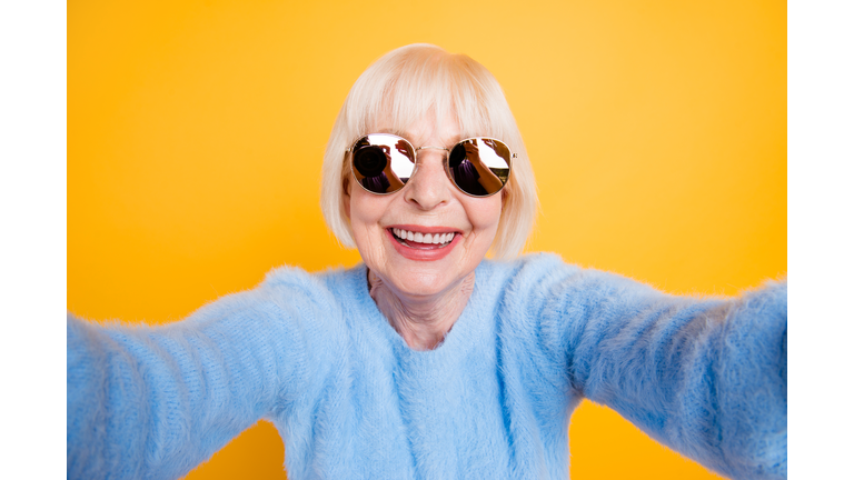 Close up portrait of happy grandma taking a selfie on vacation of two hands, isolated on yellow background