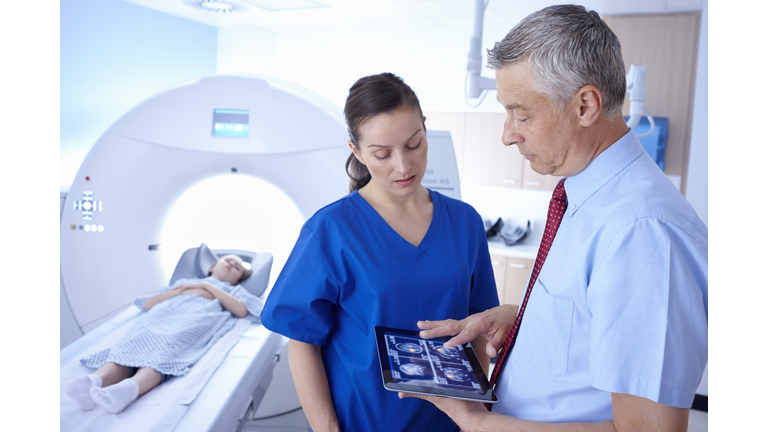 Girl in CT scanner, doctor and radiographer looking at scan on digital tablet