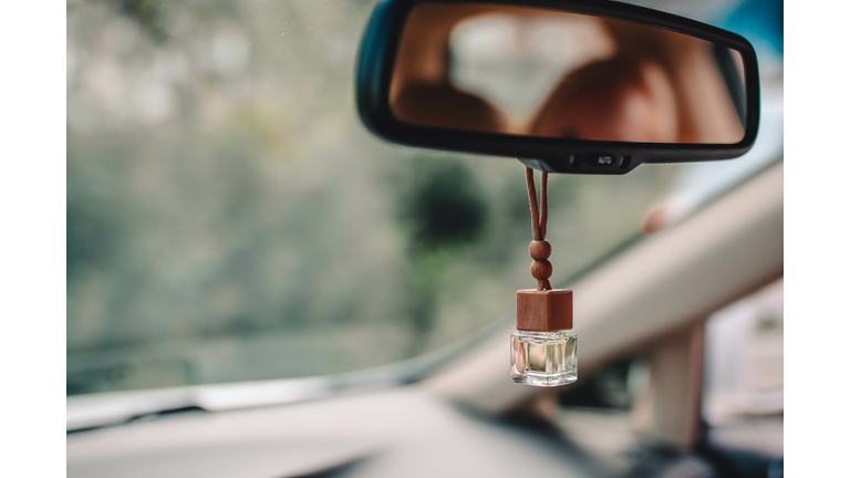 Car air parfume on the frontal mirror of the car with blurred green background outside the window.