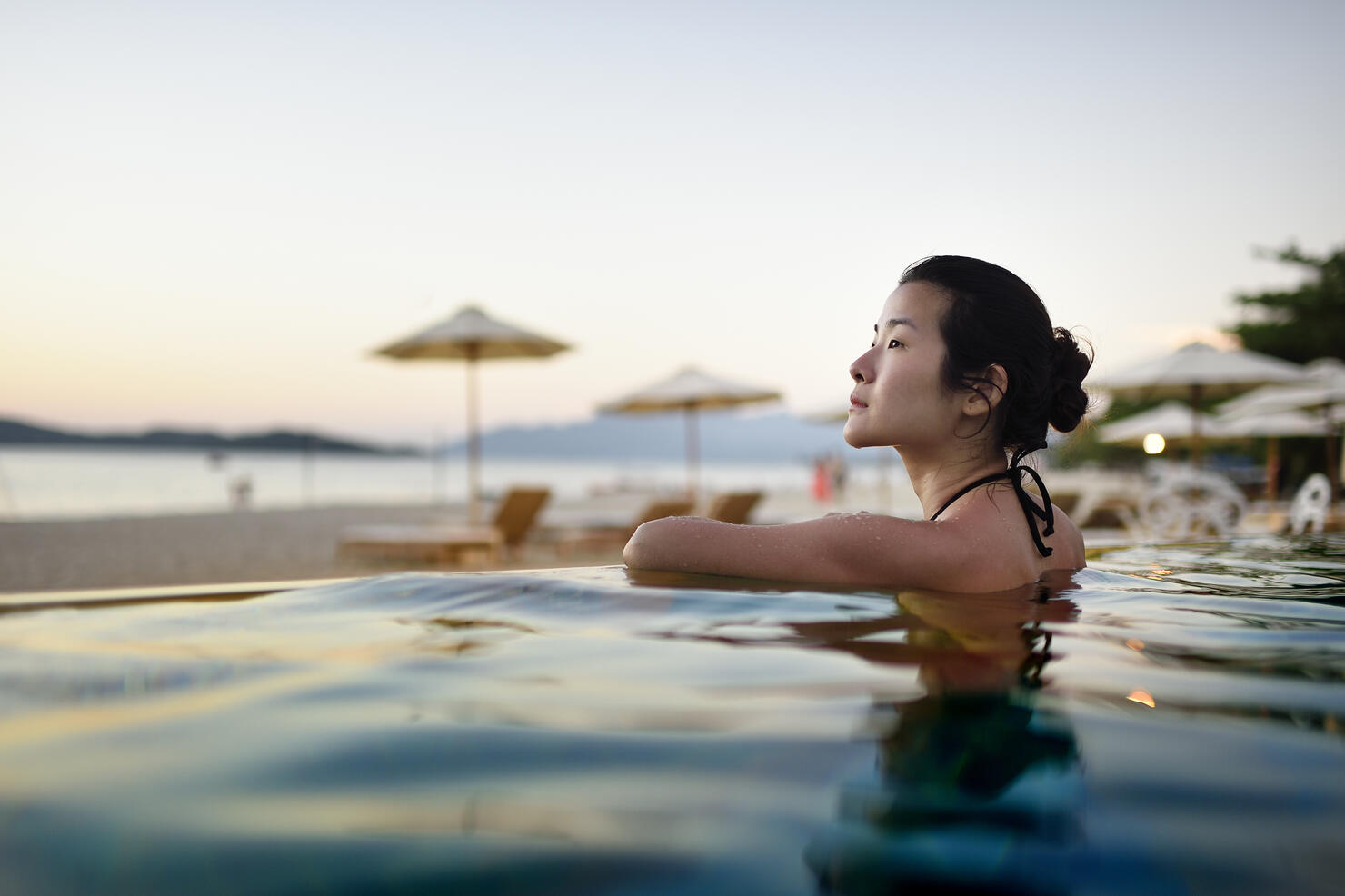 Beautiful Chinese woman in a beach resort pool at sunset