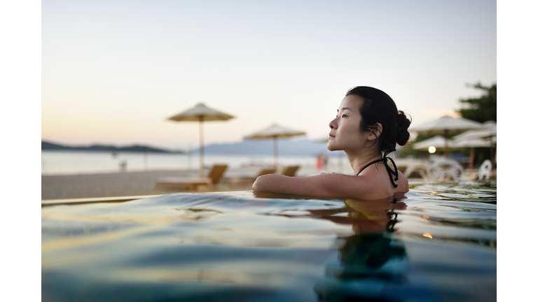 Beautiful Chinese woman in a beach resort pool at sunset