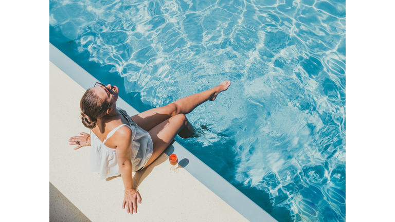 Fashionable woman sitting by the pool on the empty deck