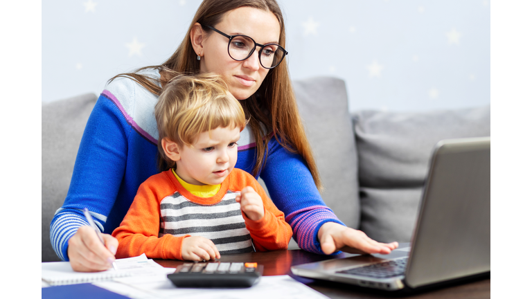 Young woman working at home with a laptop with a child on her lap