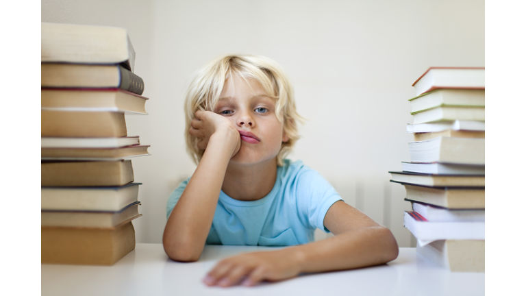 Boy sitting between two stacks of books with bored expression