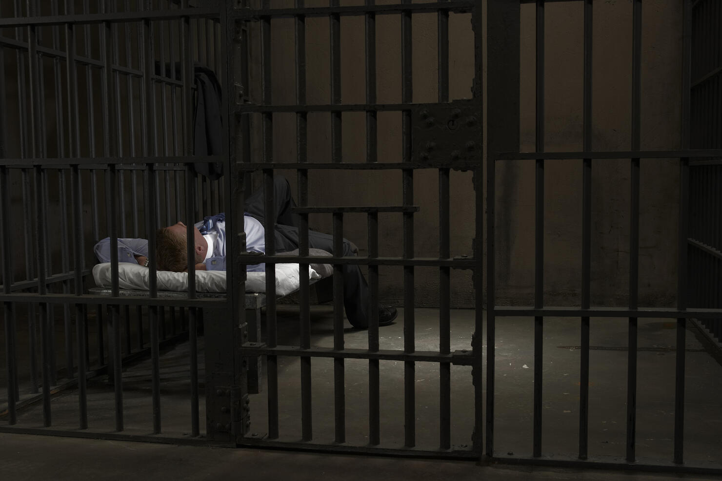 Mature man lying on bed in prison cell, rear view
