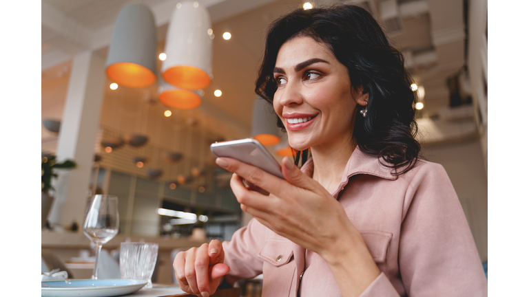 Joyful young woman talking on mobile phone in cafe