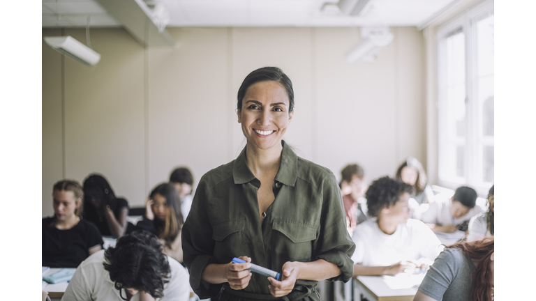 Portrait of happy female teacher with students in background at school