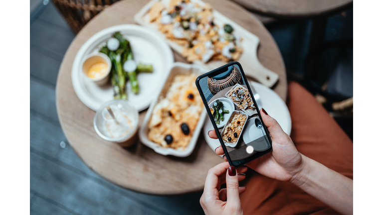 Personal perspective of young woman enjoying her home delivery takeaway meal in the balcony, taking photos of delicious food with smartphone before eating it. Eating in lifestyle. Camera eats first culture. Technology in everyday life