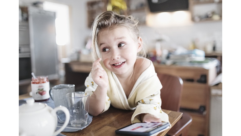 Portrait of smiling little girl with smartphone in the kitchen