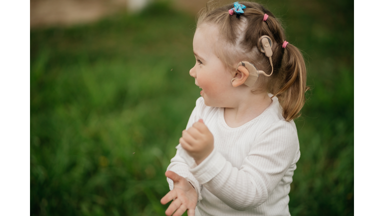 cheerful toddler girl with cochlear implants on the background green grass