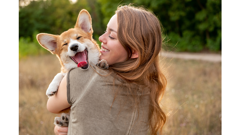 Portrait: young woman with laughing corgi puppy, nature background