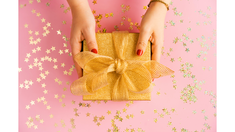 Hands of woman holding a green gift box with a yellow satin ribbon on pink background