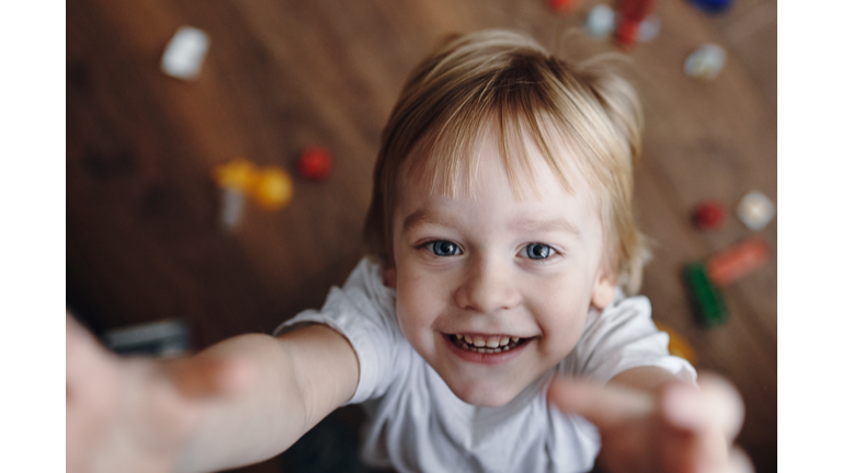 A smiling 3-year-old boy jumps and raises his hands up and looks at the camera.