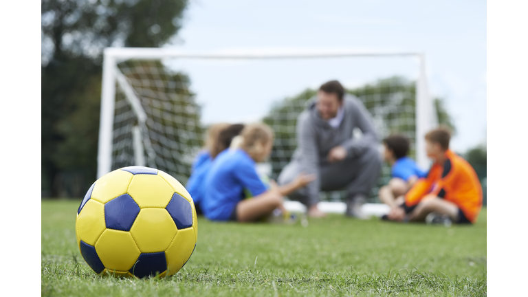 Coach  And Team Discussing Soccer Tactics With Ball In Foregroun