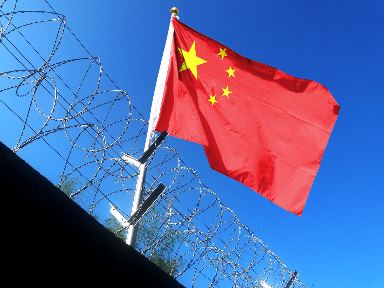 The Chinese flag hangs in the cloudy sky outside the prison's barbed wire. waving in the sky