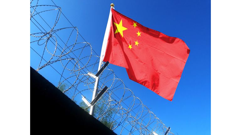 The Chinese flag hangs in the cloudy sky outside the prison's barbed wire. waving in the sky