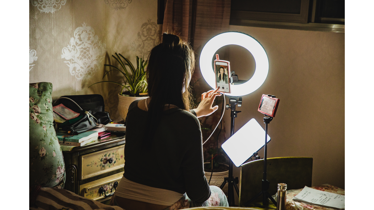 asian female influencer filming content using phone in a bedroom