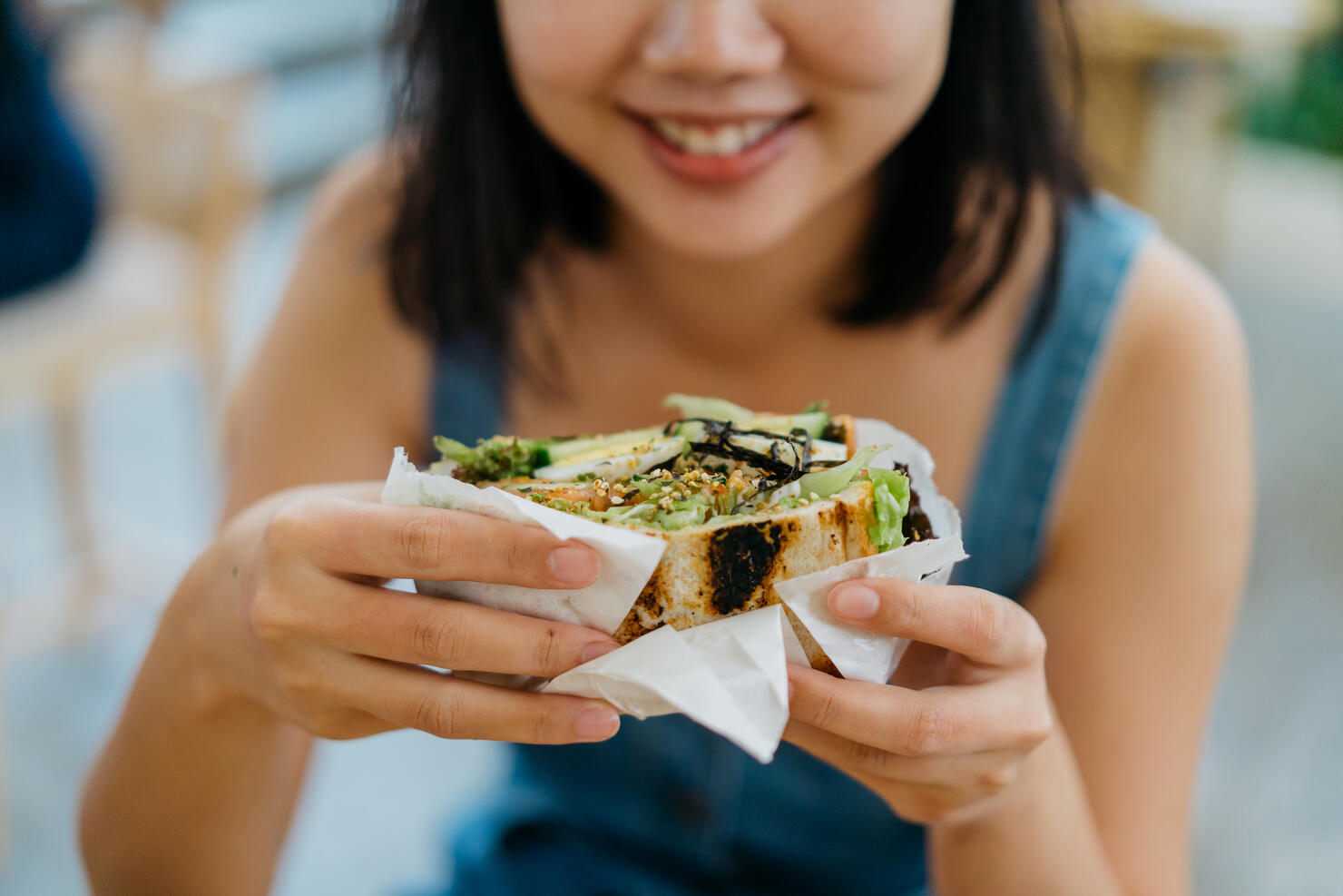 Young asian woman eating sandwich in cafe