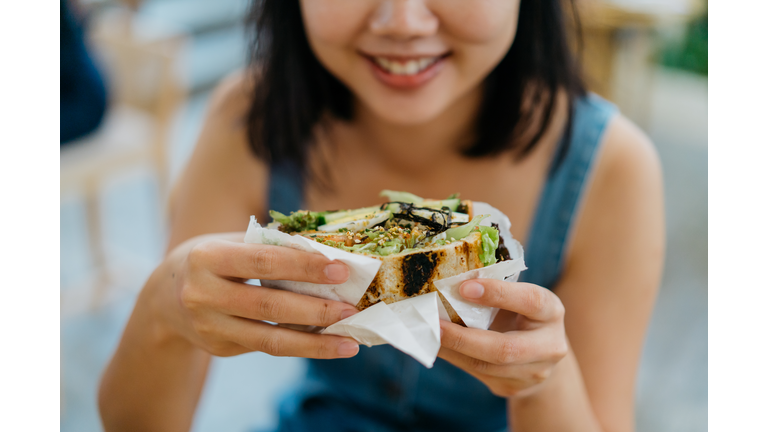 Young asian woman eating sandwich in cafe
