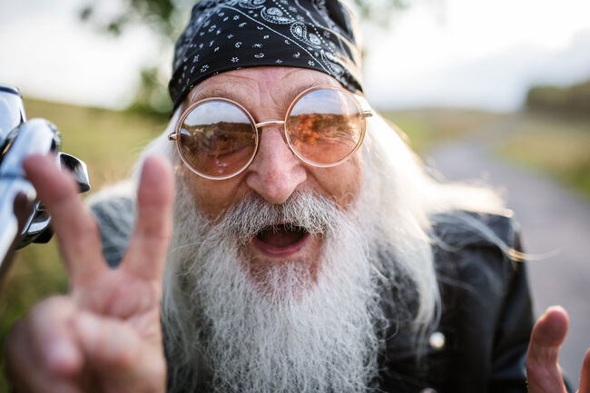 Portrait of senior man rider with motorbike in the countryside, having fun.