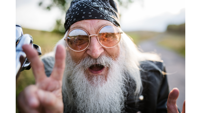 Portrait of senior man rider with motorbike in the countryside, having fun.