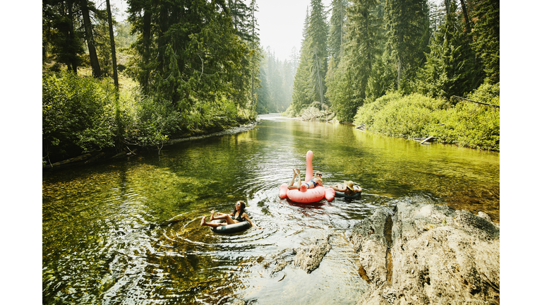 Laughing female friends floating down river on inner tubes and pink flamingo on summer afternoon