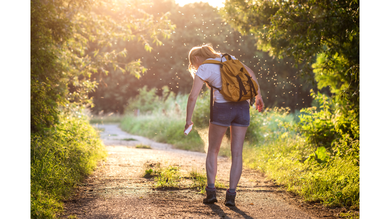 Woman with backpack applying insect repellent agains mosquito and tick outdoors