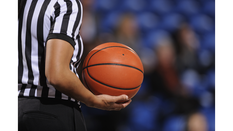 Faceless female basketball referee holds ball in one hand