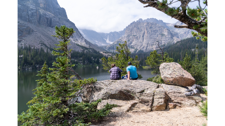 Man and woman hiker couple sit, relax and enjoy the view of Loch Vale lake in Rocky Mountain National Park