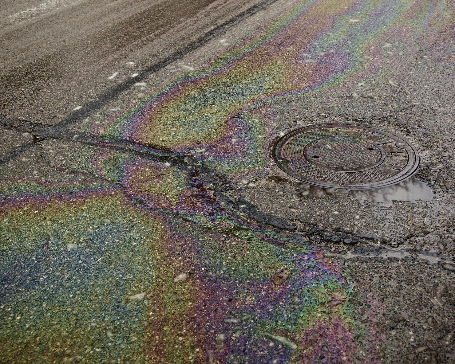 Oil on a wet, cracked road near a manhole