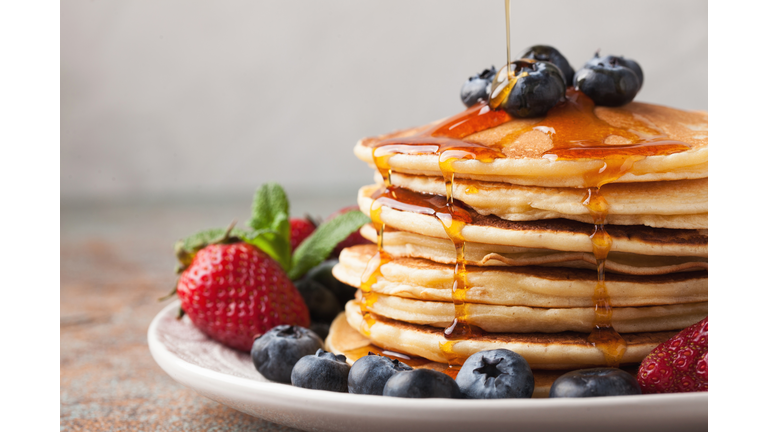 Close-up delicious pancakes, with fresh blueberries, strawberries and maple syrup on a light background. With copy space. Sweet maple syrup flows from a stack of pancake