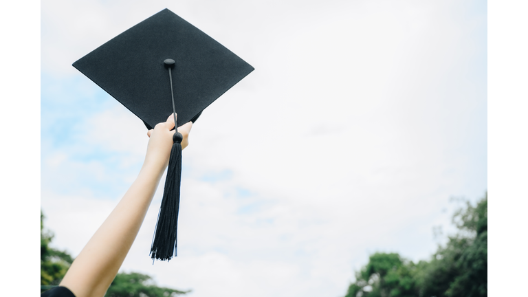 Student hand celebrating graduation by holding and throwing cap against the sky.