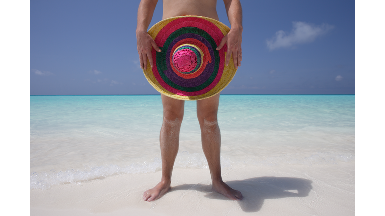 Naked man holding a sombrero on tropical beach