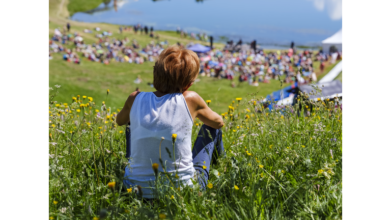 Elderly woman sitting in a meadow listens to a music concert.