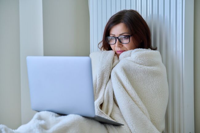 Woman working at home with laptop, warming with blanket and heating radiator