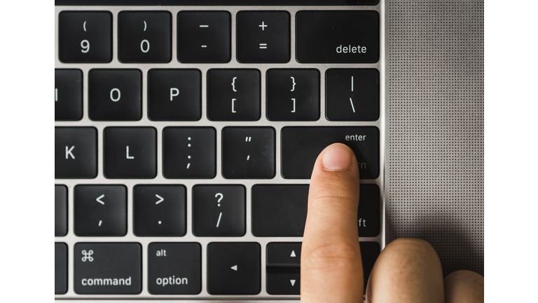 Overhead view of cropped finger pressing enter key on laptop computer's keyboard
