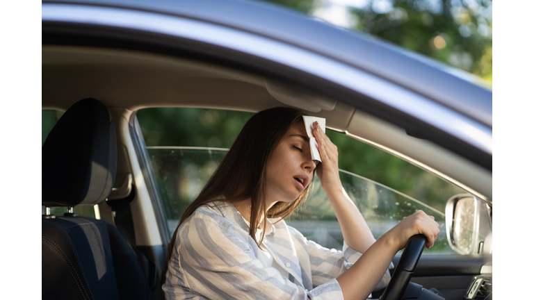 Woman driver being hot during heat wave in car, suffering from hot weather wipes sweat from forehead