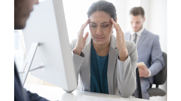 Businesswoman with headache rubbing temples in office