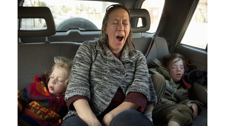 Exhausted mother yawns while her daughters sleep.